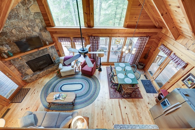 living room with beam ceiling, hardwood / wood-style floors, high vaulted ceiling, and a stone fireplace