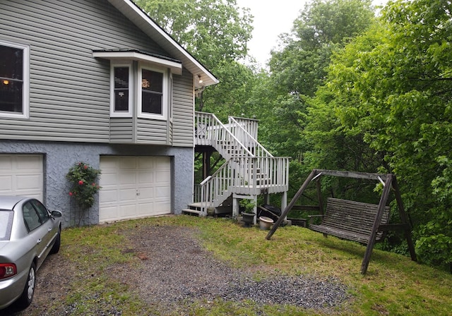 view of side of home featuring stucco siding, an attached garage, stairs, and dirt driveway