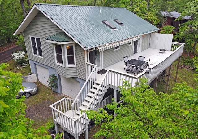 rear view of house featuring metal roof, outdoor dining area, a deck, stairway, and an attached garage