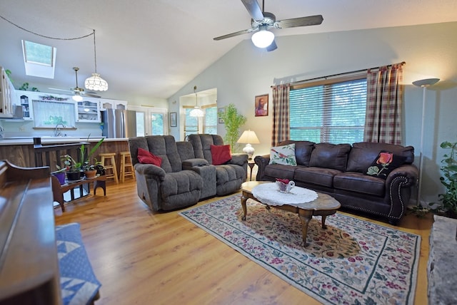 living room with ceiling fan, a skylight, high vaulted ceiling, and light wood-type flooring