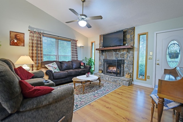 living area featuring a ceiling fan, a fireplace, vaulted ceiling, wood finished floors, and baseboards