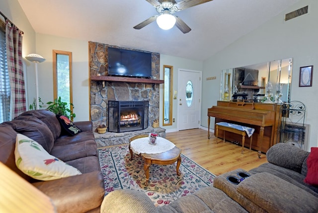 living area with a ceiling fan, visible vents, a fireplace, vaulted ceiling, and wood finished floors