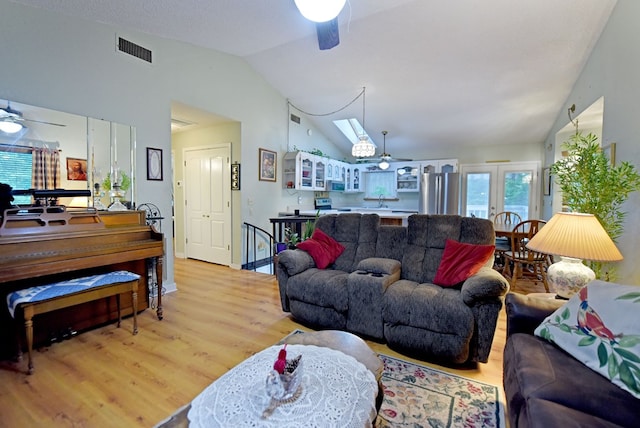 living room featuring vaulted ceiling with skylight, a ceiling fan, light wood-type flooring, and visible vents