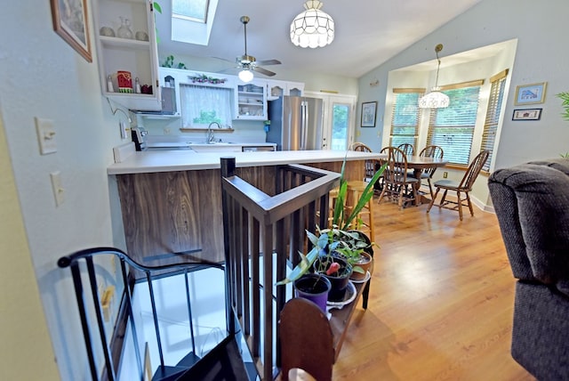 kitchen featuring a sink, light wood finished floors, vaulted ceiling with skylight, freestanding refrigerator, and a peninsula