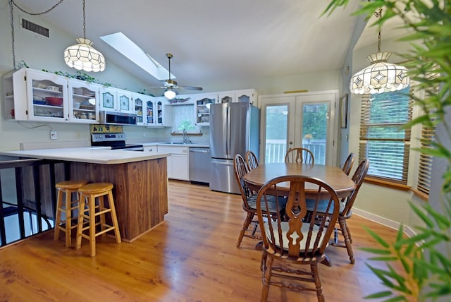kitchen featuring glass insert cabinets, appliances with stainless steel finishes, a peninsula, and lofted ceiling with skylight