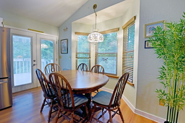 dining area with an inviting chandelier, a textured wall, wood finished floors, and lofted ceiling