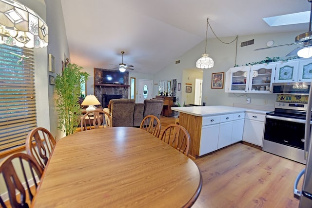 dining space featuring light wood-style floors, a fireplace, a ceiling fan, and visible vents