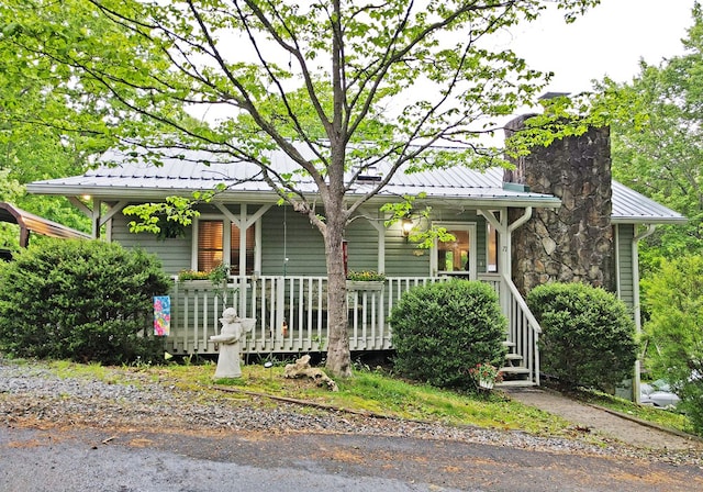 view of front of property featuring covered porch, a standing seam roof, a chimney, and metal roof