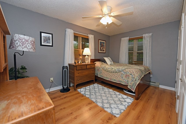 bedroom with a textured ceiling, baseboards, a baseboard heating unit, and wood finished floors