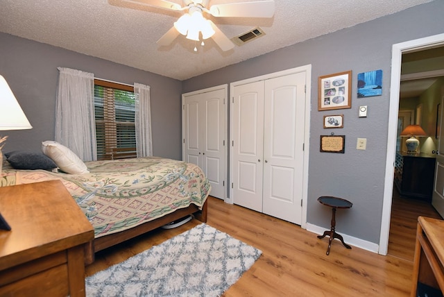 bedroom with two closets, light wood finished floors, a textured ceiling, and visible vents