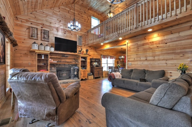 living room with high vaulted ceiling, hardwood / wood-style flooring, a notable chandelier, wood walls, and visible vents