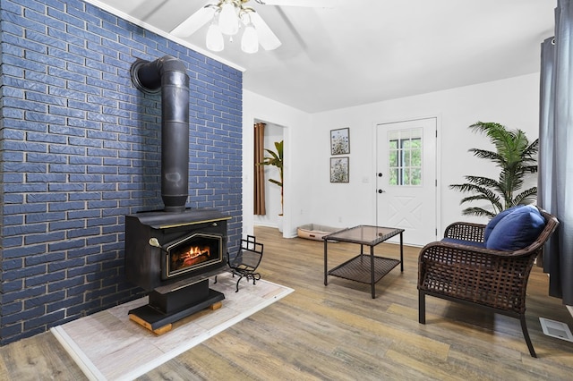 living room featuring hardwood / wood-style flooring, brick wall, ceiling fan, and a wood stove