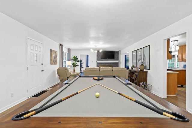 rec room with hardwood / wood-style flooring, a brick fireplace, an inviting chandelier, and billiards