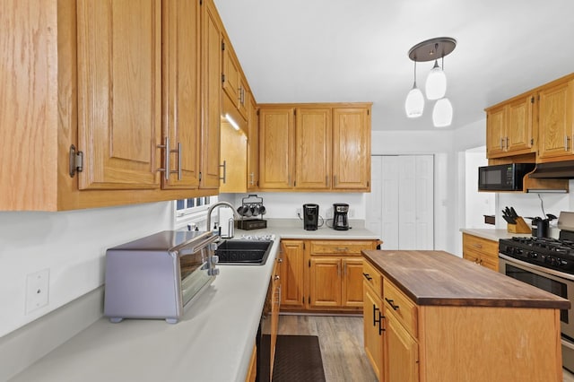 kitchen with sink, hanging light fixtures, a center island, light hardwood / wood-style floors, and gas stove