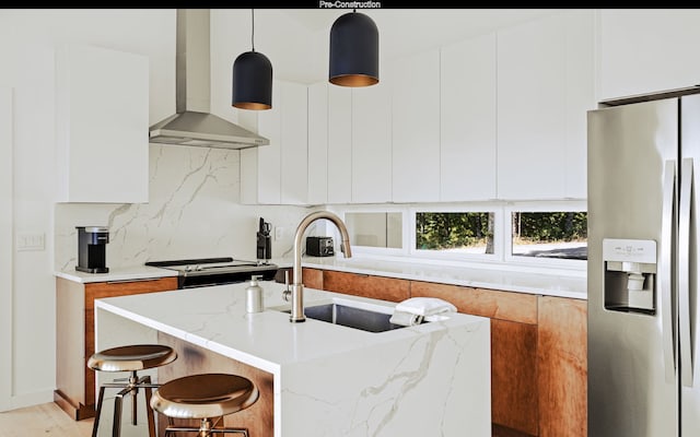 kitchen featuring light stone counters, white cabinets, pendant lighting, stainless steel fridge, and wall chimney range hood