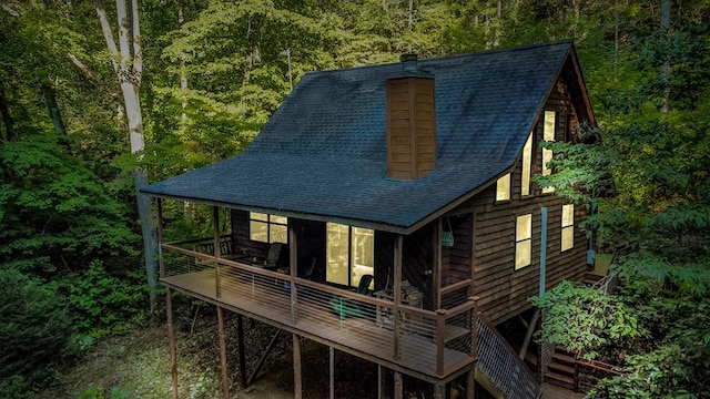 rear view of property featuring a deck, roof with shingles, a chimney, and a view of trees