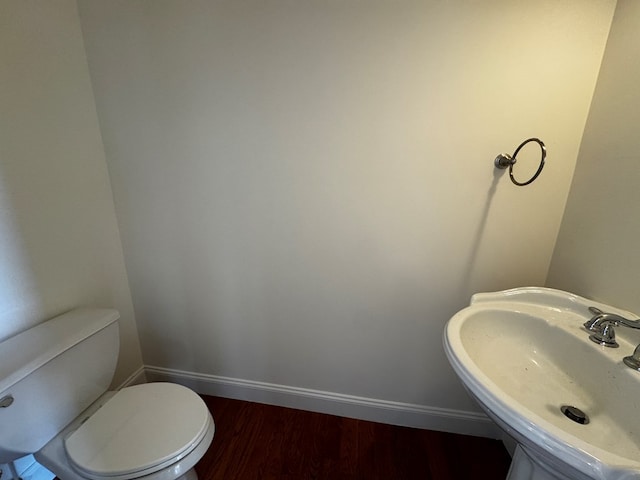 half bath featuring wood finished floors, a sink, toilet, and baseboards