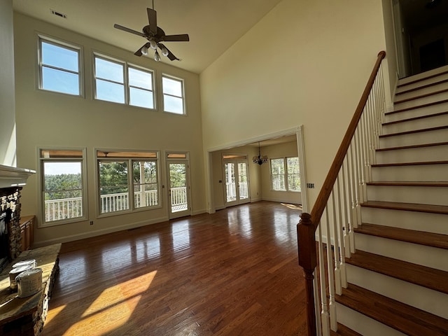 living room with baseboards, a fireplace with raised hearth, wood finished floors, stairs, and ceiling fan with notable chandelier