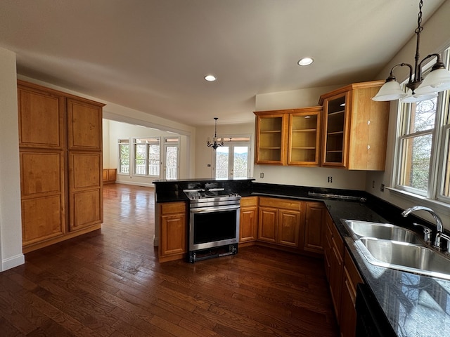 kitchen with dark wood-style floors, brown cabinetry, a sink, stainless steel gas range, and a peninsula