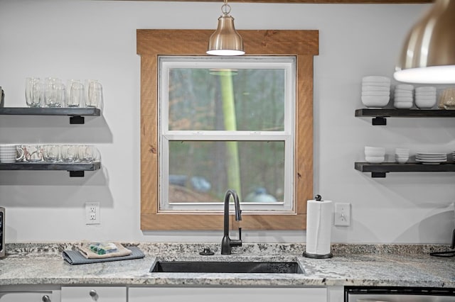 interior space featuring light stone counters, stainless steel dishwasher, sink, and hanging light fixtures