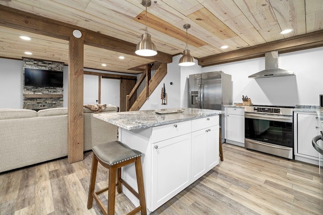 kitchen featuring wall chimney exhaust hood, white cabinetry, hanging light fixtures, stainless steel appliances, and a kitchen island with sink