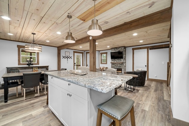 kitchen featuring white cabinetry, hanging light fixtures, a center island, light stone counters, and wooden ceiling