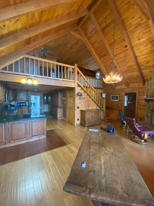 interior space with ceiling fan with notable chandelier, wooden walls, beamed ceiling, wood ceiling, and light hardwood / wood-style flooring