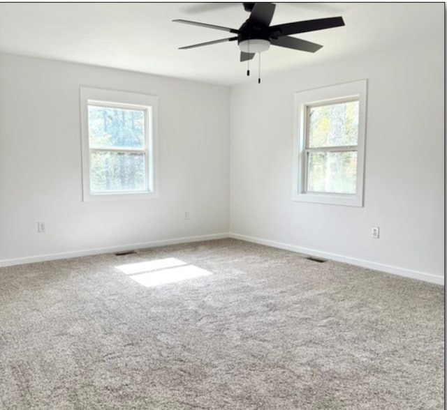 carpeted empty room featuring ceiling fan, baseboards, and a wealth of natural light