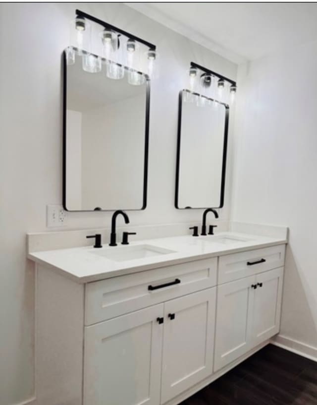 full bathroom with double vanity, a sink, baseboards, and wood finished floors