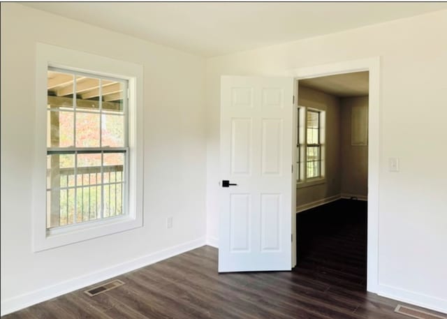 unfurnished room featuring dark wood finished floors, visible vents, and baseboards