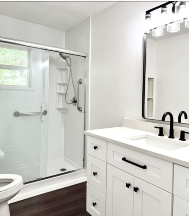 bathroom with toilet, a stall shower, wood finished floors, and vanity