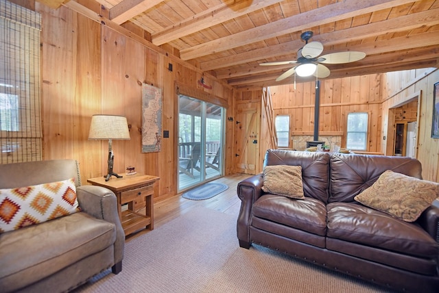 living room featuring beamed ceiling, a wood stove, ceiling fan, hardwood / wood-style floors, and wooden walls