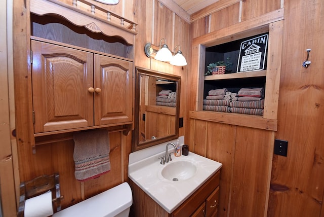 half bath featuring toilet, built in shelves, wooden walls, and vanity