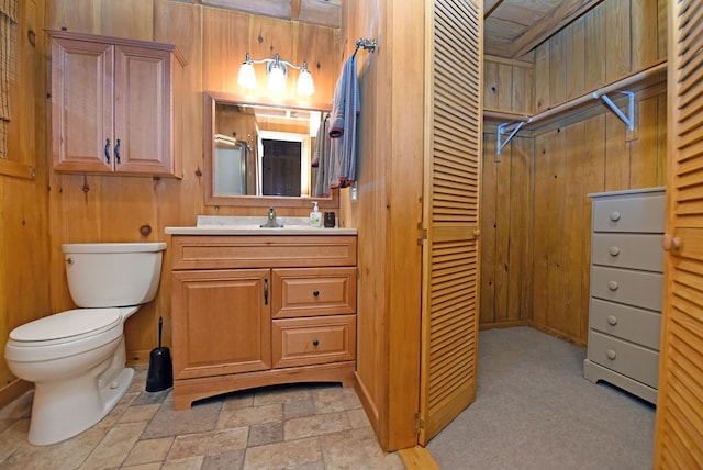full bath with stone finish floor, a closet, toilet, vanity, and wooden walls