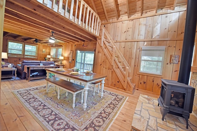 dining space with wood walls, a ceiling fan, hardwood / wood-style floors, and a wood stove