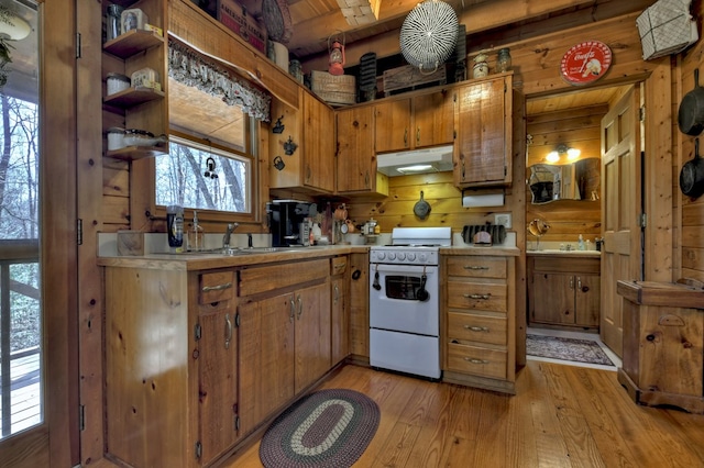 kitchen with under cabinet range hood, light countertops, white range oven, light wood-style floors, and a sink