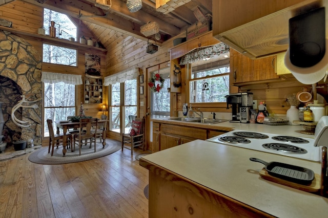 kitchen with light wood-type flooring, beam ceiling, a sink, light countertops, and cooktop