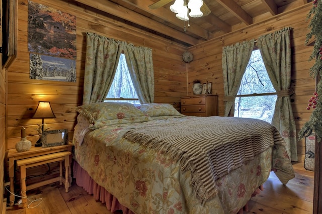 bedroom with beamed ceiling, wood walls, multiple windows, and hardwood / wood-style floors