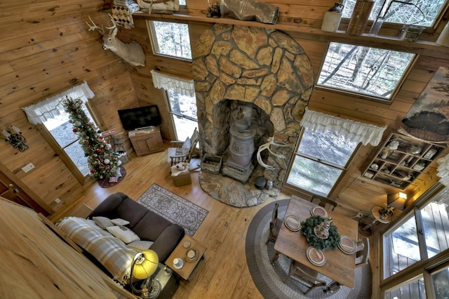 living area featuring a stone fireplace, a towering ceiling, wood walls, and hardwood / wood-style floors