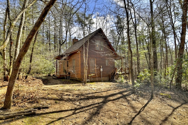 view of side of home with a wooded view and a chimney