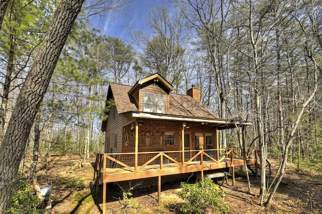 exterior space with a wooden deck, a chimney, and a shingled roof