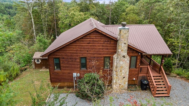 view of side of home featuring stairway, metal roof, a chimney, and a forest view