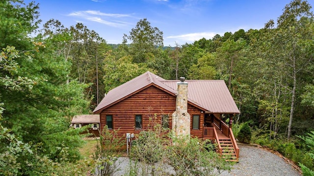 view of side of property featuring metal roof, a forest view, and a chimney