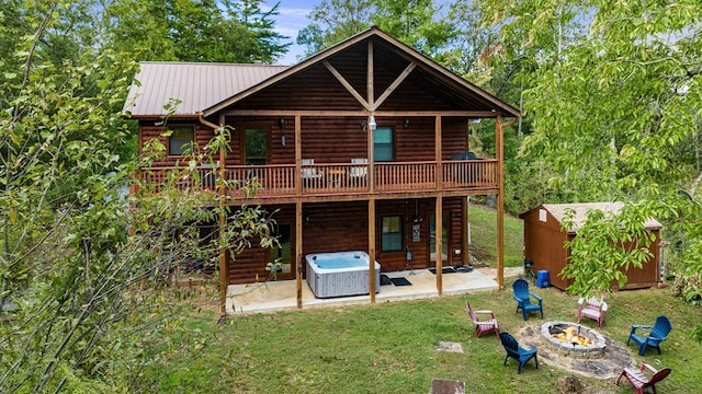 back of house featuring an outbuilding, a storage unit, a hot tub, a patio area, and a fire pit