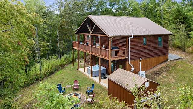 rear view of house featuring a hot tub, a lawn, log veneer siding, a deck, and a patio area