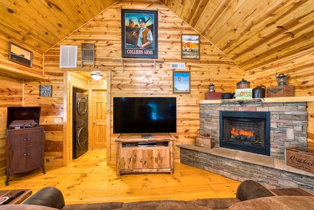 living room featuring wood ceiling, light hardwood / wood-style flooring, stacked washer and clothes dryer, and a stone fireplace