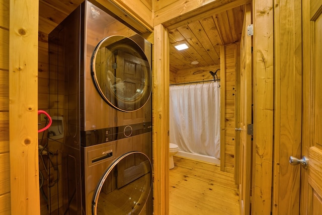 clothes washing area featuring wood ceiling, light hardwood / wood-style flooring, stacked washer and dryer, and wooden walls