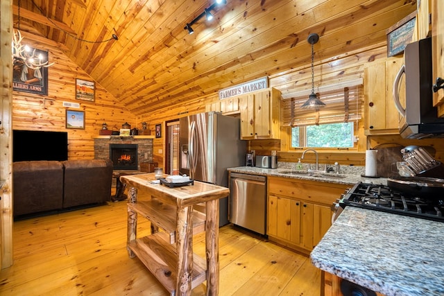 kitchen featuring vaulted ceiling, pendant lighting, appliances with stainless steel finishes, sink, and wooden walls