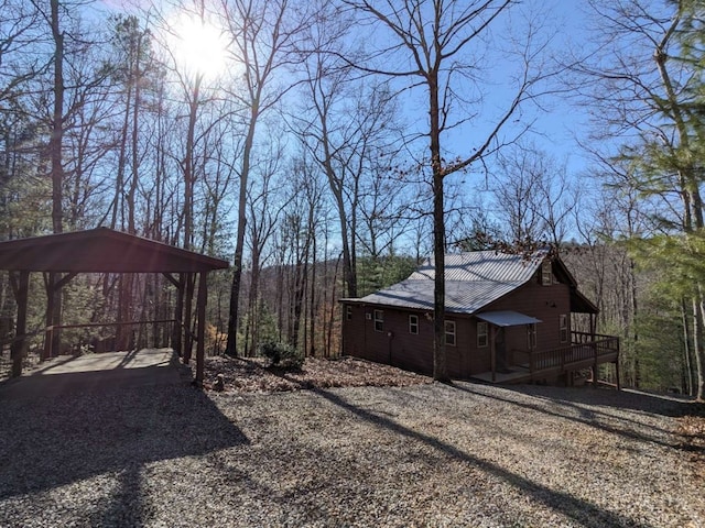 view of yard with a carport, dirt driveway, a view of trees, and a wooden deck