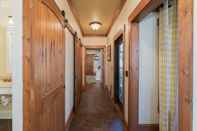 corridor featuring a barn door, a textured ceiling, and crown molding